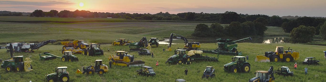 Personas que caminan entre distintos tipos de equipos de John Deere en un gran campo.