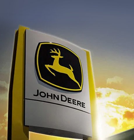 Un letrero con el logotipo de John Deere delante de un edificio durante una puesta de sol
