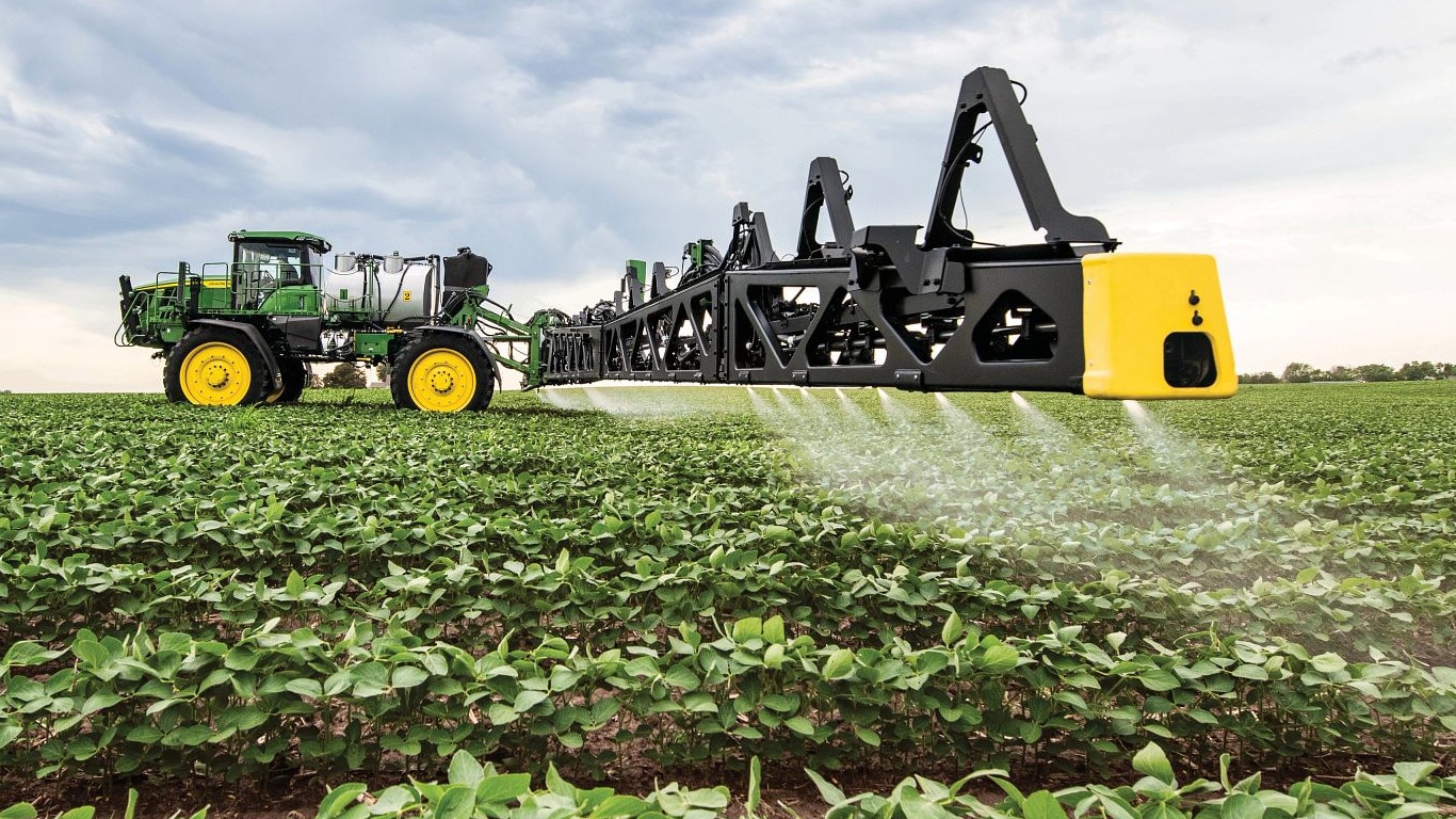 Vista en primer plano del brazo de un pulverizador de John Deere en un campo abierto.