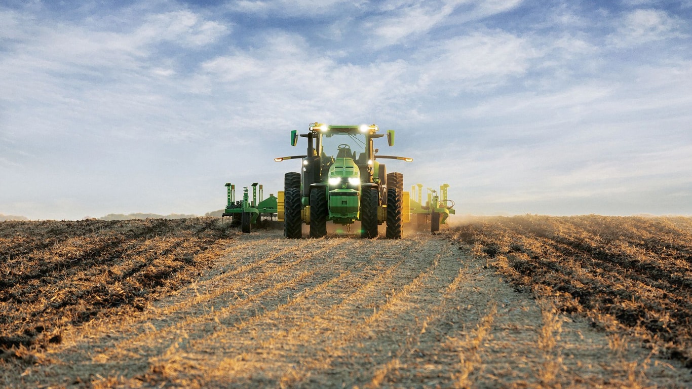 Tractor John Deere autónomo que tira del equipo de laboreo a través de un campo abierto.