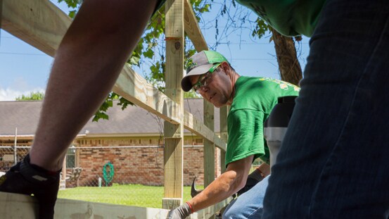 Dos personas construyendo juntas una cerca junto a un edificio.