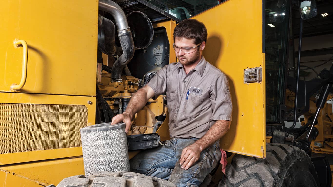 Un hombre con gafas de protección trabaja en un motor John Deere dentro de una máquina de equipo pesado