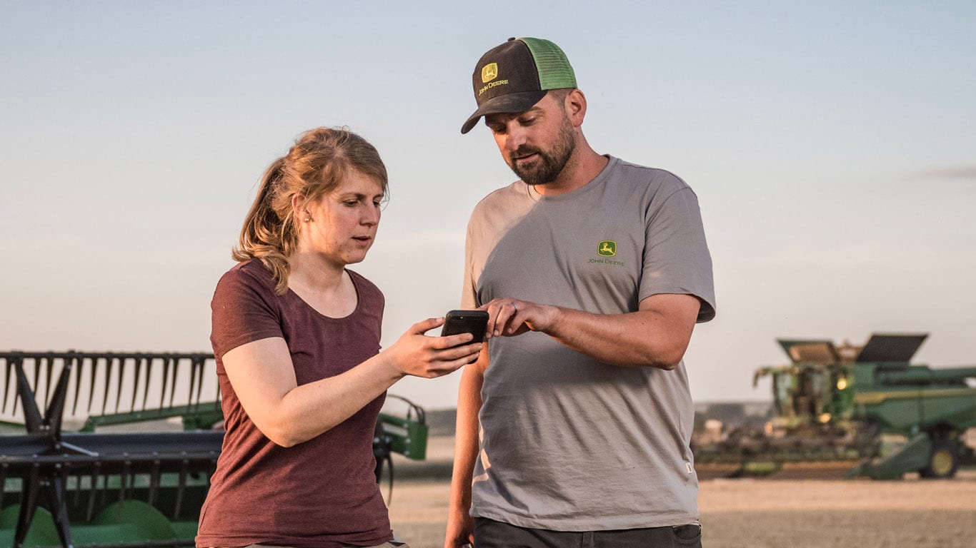 Dos personas al aire libre, una sosteniendo un teléfono inteligente mientras la otra apunta a la pantalla