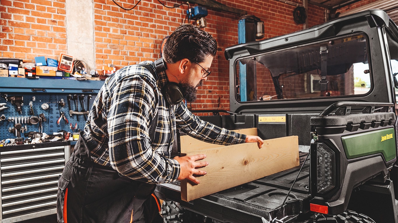 Hombre reconfigurando la caja de transporte y almacenamiento de un Gator™ XUV 875M con madera estándar