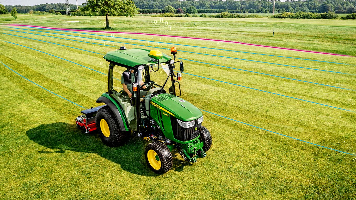 Un encargado del mantenimiento de espacios verdes trabaja en una zona de césped con un tractor compacto John Deere.