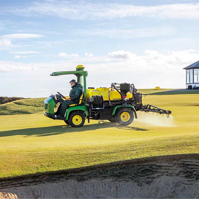 Un encargado de mantenimiento trabaja en una zona verde con un pulverizador John Deere