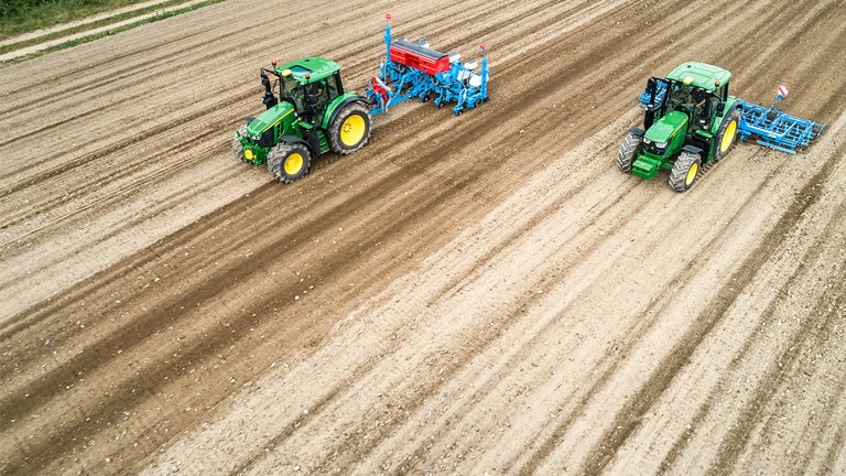 Dos tractores John Deere 6M en un campo de tierra desnuda. Uno est&aacute; tirando de una sembradora Monsomen. El otro est&aacute; tirando de una combinaci&oacute;n de sementeras Lemken