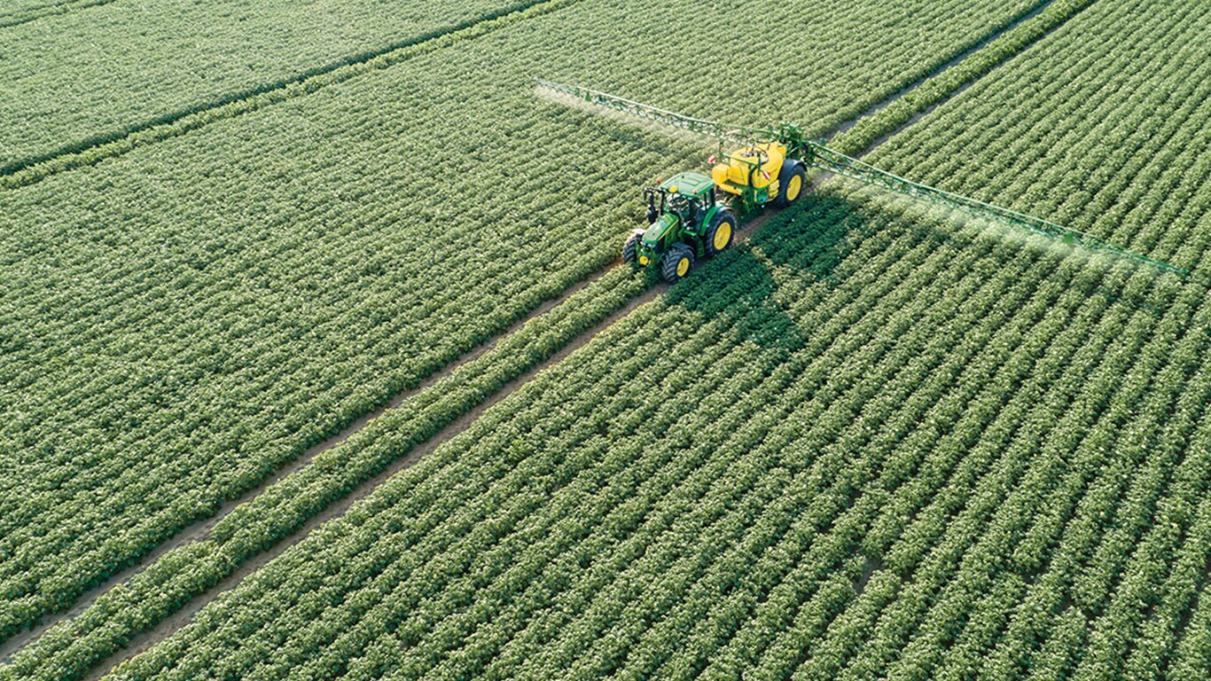 Tractor John Deere Serie 6M tirando de un pulverizador remolcado M700 en un campo de patatas