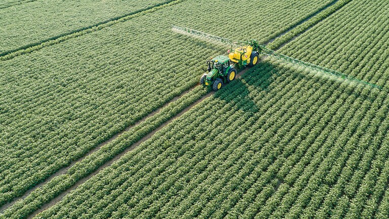 Tractor John Deere Serie 6M tirando de un pulverizador remolcado M700 en un campo de patatas
