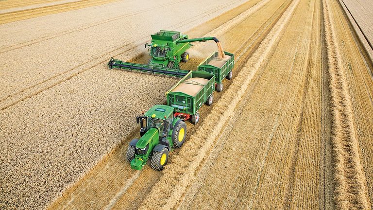 Cosechadora de la serie S John Deere descarga trigo en un remolque doble tirada por un tractor