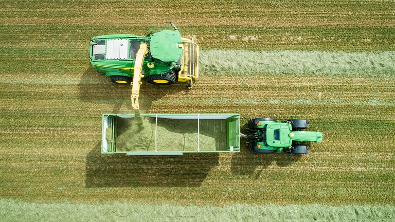 Foto a&eacute;rea de la cosechadora autopropulsada de la serie 8000 John Deere con un recogedor de hierba de carga del ensilado en un carro tirado por un tractor John Deere