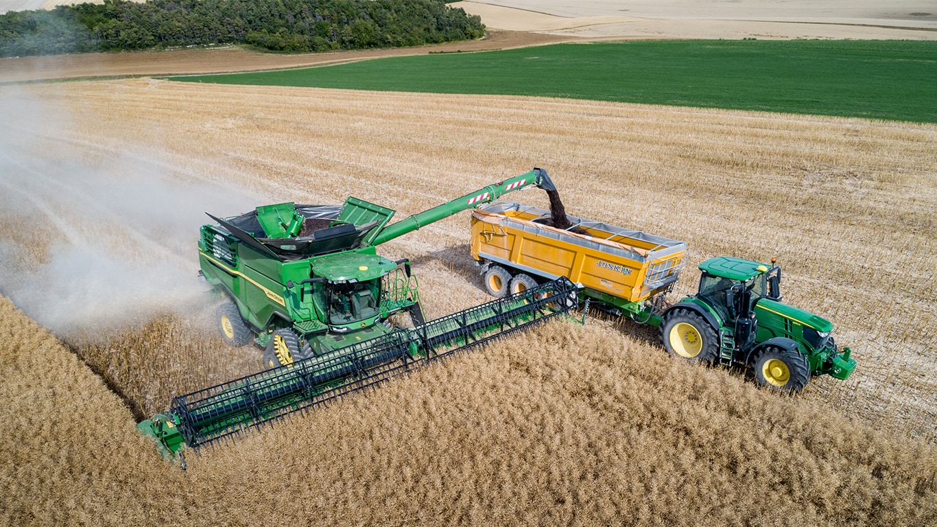 Cosechadora John Deere Serie X descargando semilla de colza en un carro de grano tirada por un tractor John Deere